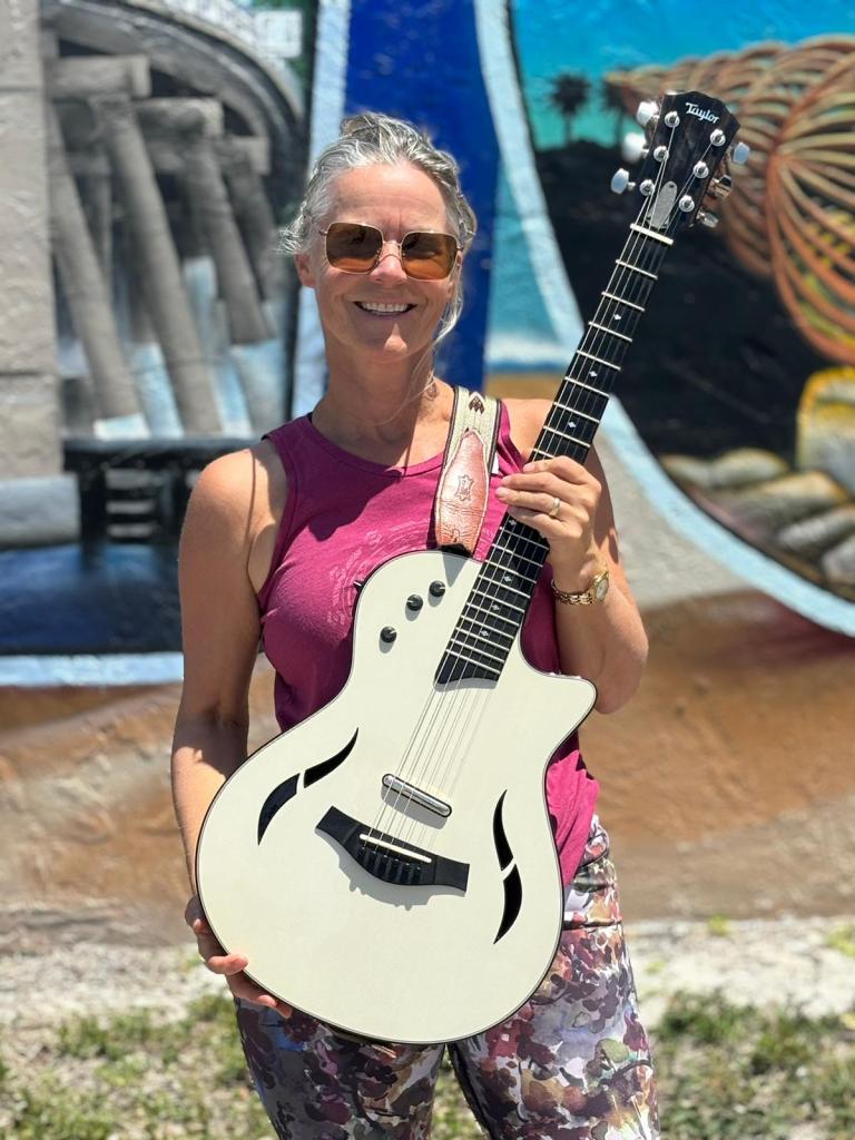 Katja standing in front of a painting with Taylor TZ5 guitar 